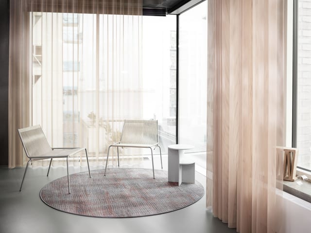 A round rug under two lounge chairs by a window