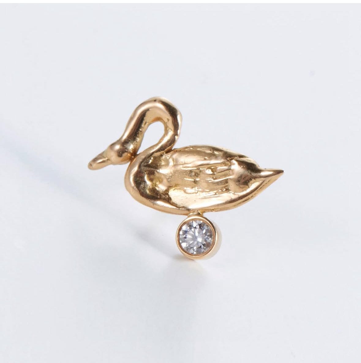 The Aphrodite earring, a gold swan above a set diamond
