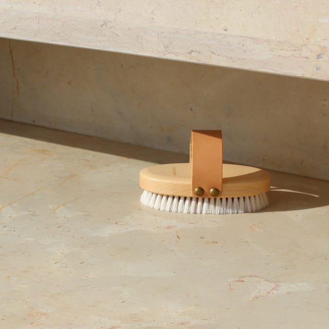 BUFF brush with pale bristles and its leather strap on stone