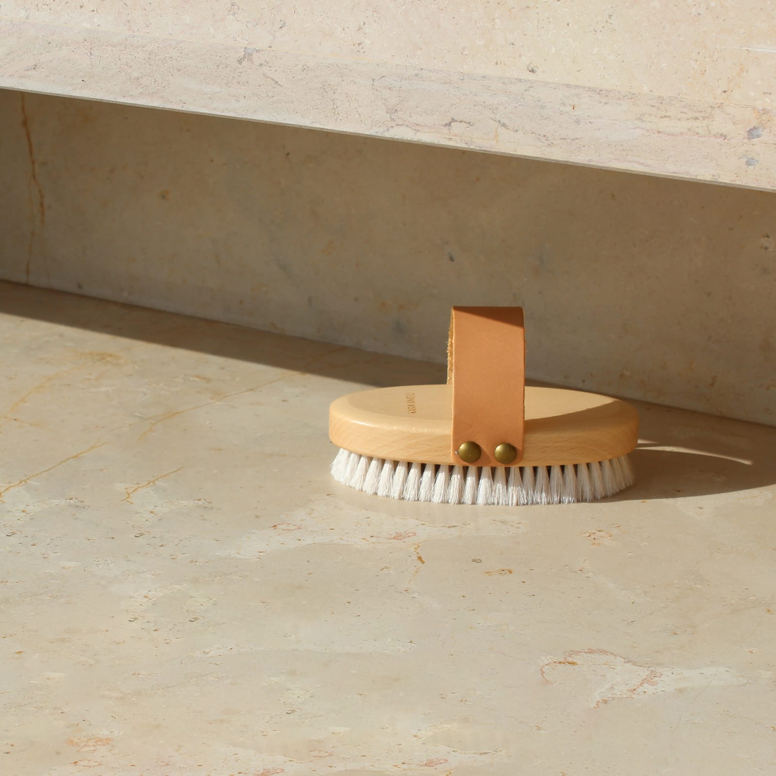 BUFF brush with pale bristles and its leather strap on stone