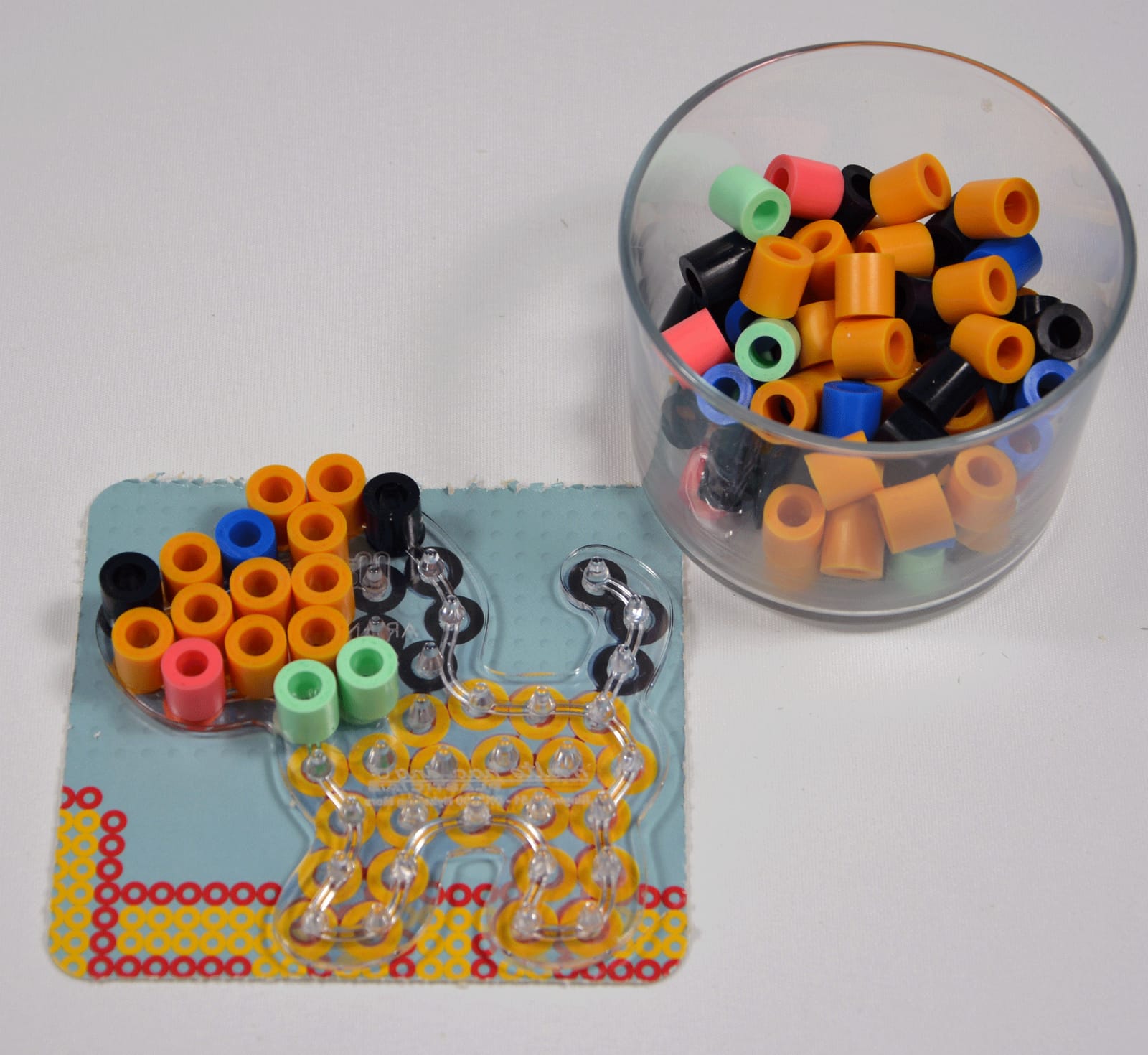 Maxi beads in a glass beside a dog-shaped pegboard being filled