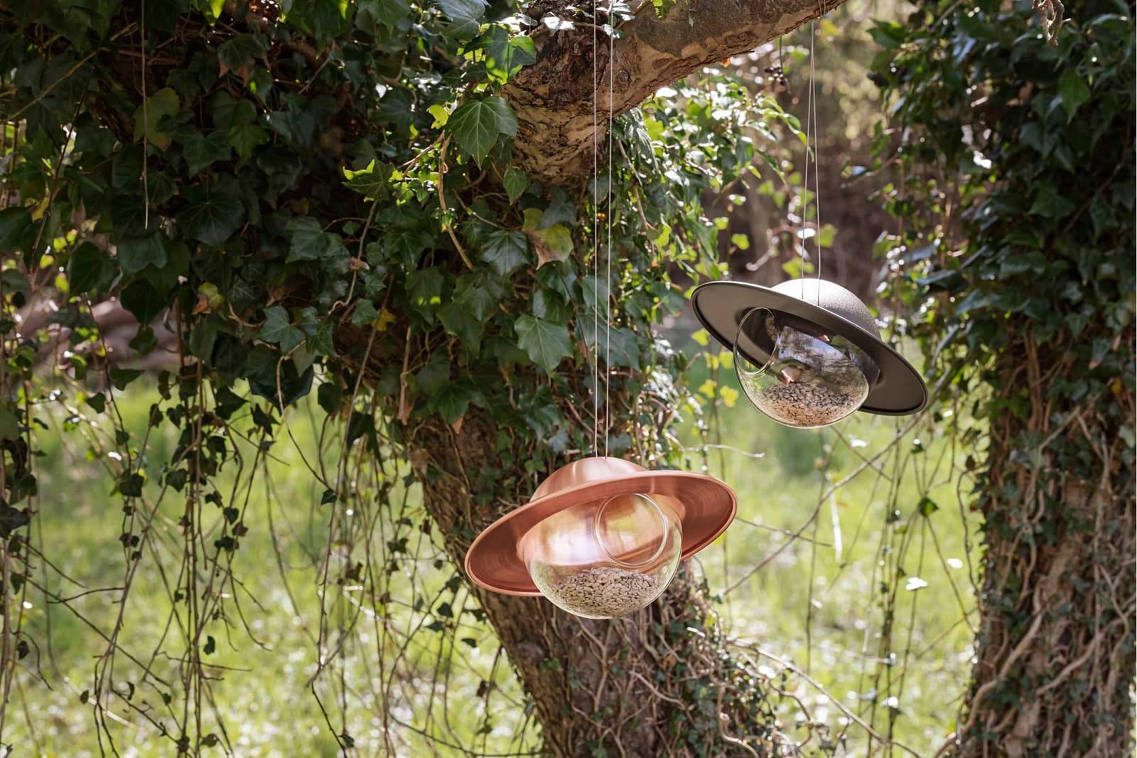 Two Saturn glass bird feeders hanging from a tree
