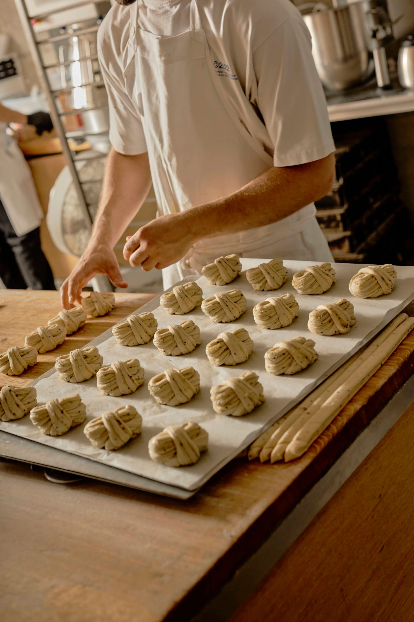A baker shaping buns on a tray