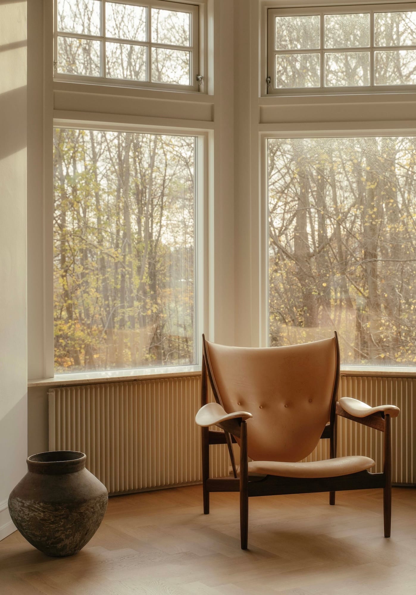A Chieftain Chair in walnut and natural leather by a window