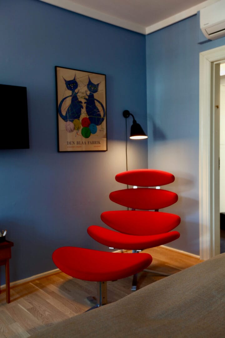 A blue guest room with a red lounge chair