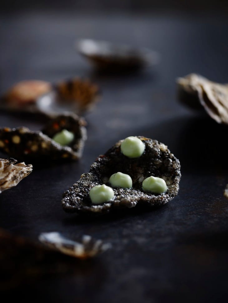 A snack of green dots on a black cracker