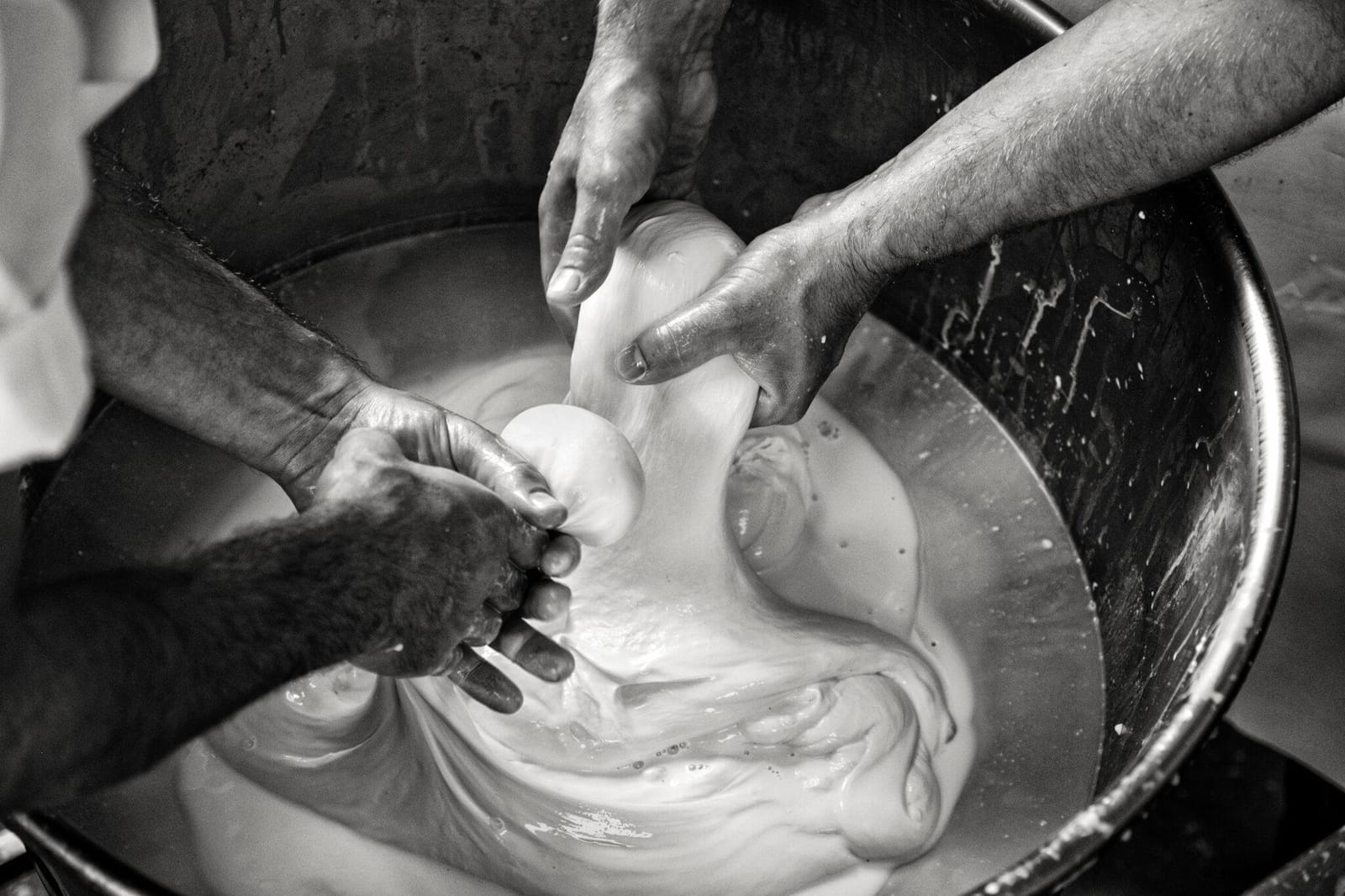 Mozzarella being stretched by hand in a bowl