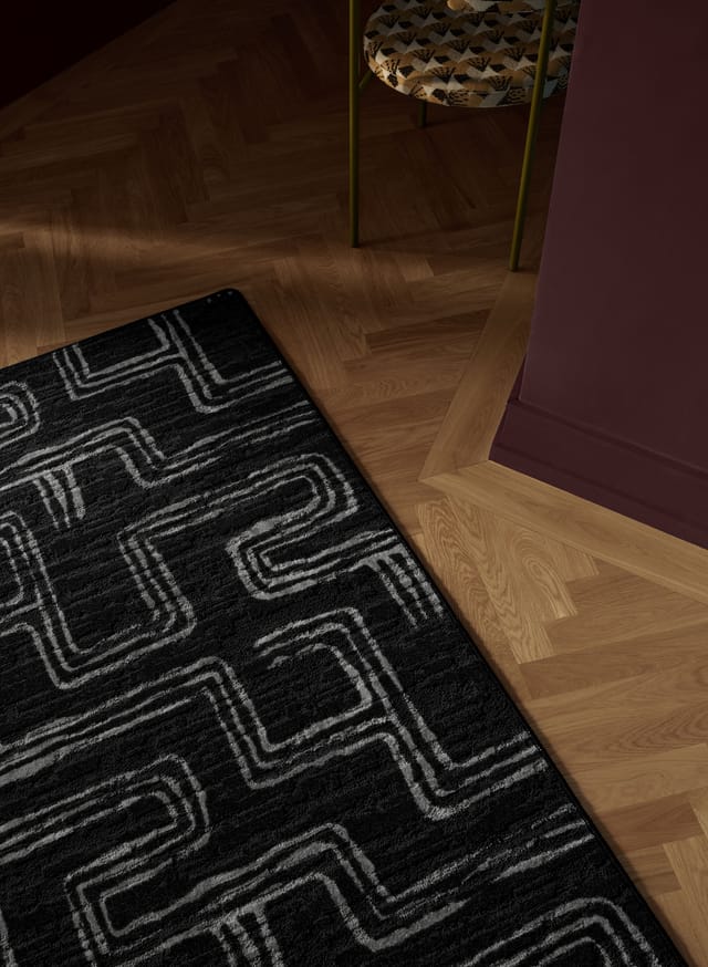 A black rug with a grey pattern on a parquet floor