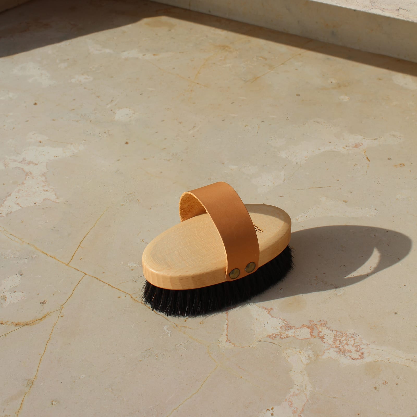RECHARGE brush with dark bristles and leather strap on stone