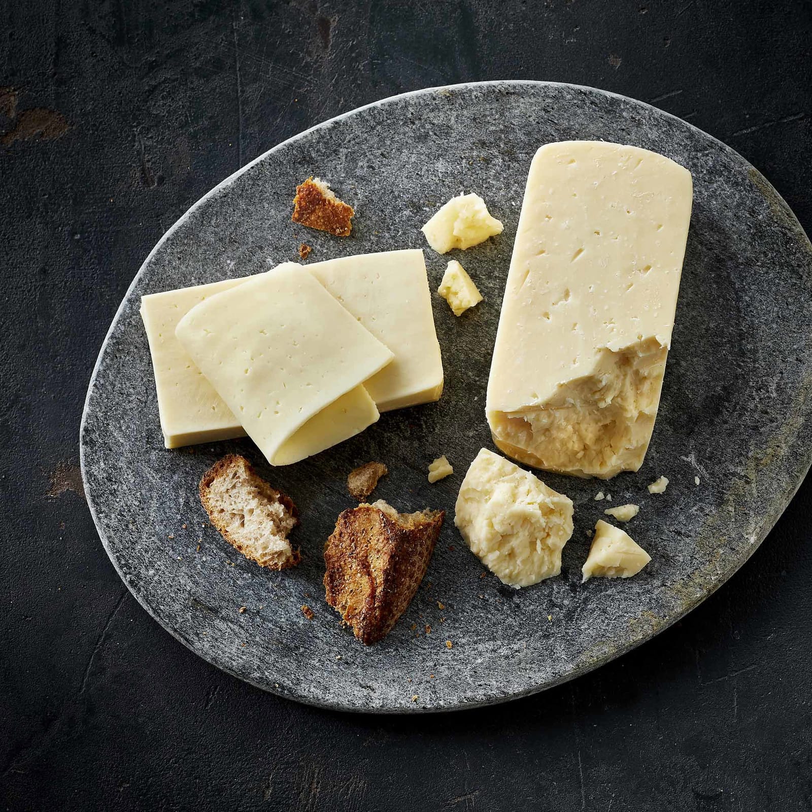 Slices and an aged piece of Havarti on a stone board