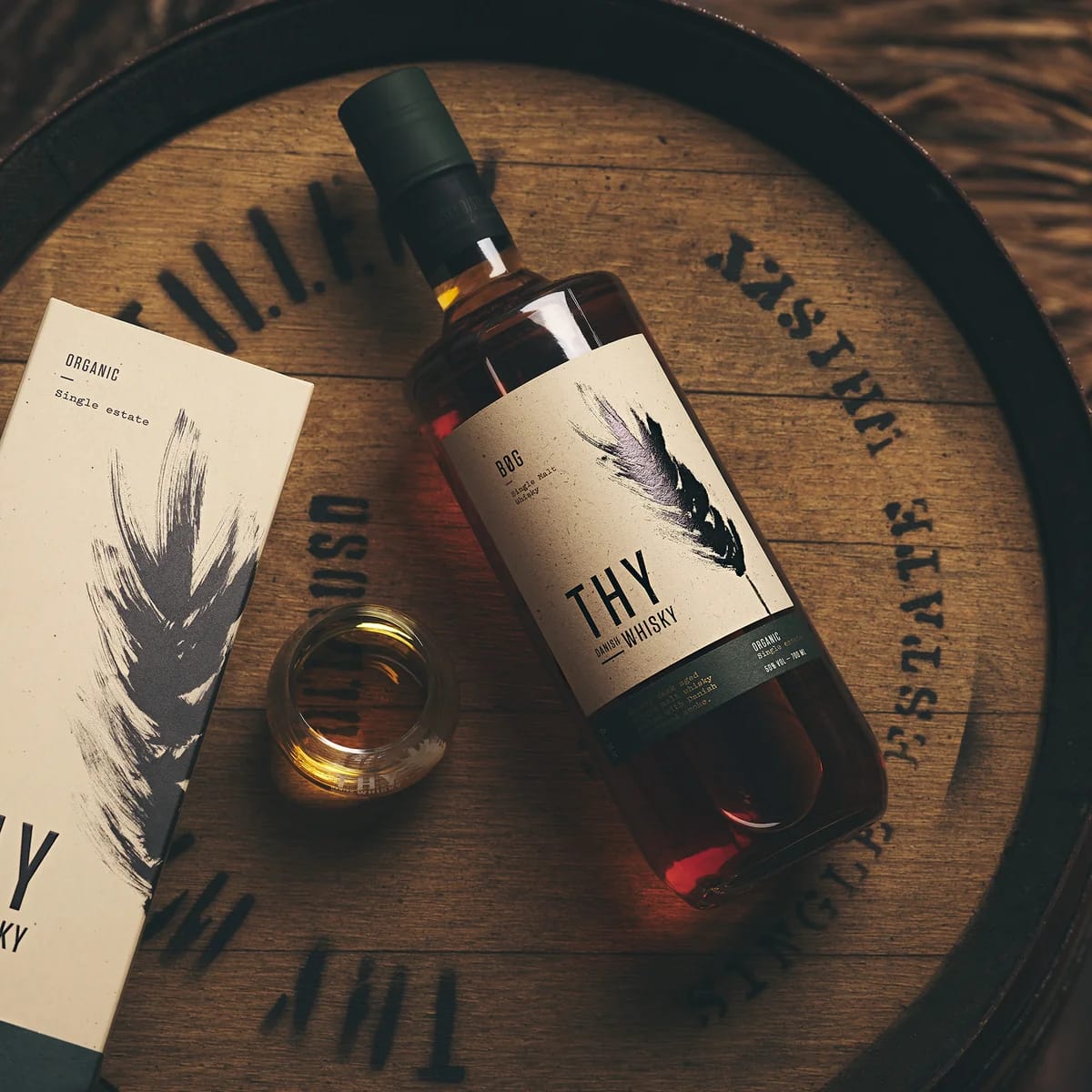 A bottle of Bøg single malt on a cask head, beside its box and a glass